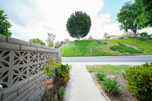 a concrete wall next to a road and a lush green hillside